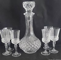 Full view of decanter centered with stopper on, flanked by three stemmed sherry glasses on each side, showing diamond cut pattern on all the glass pieces.