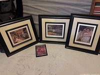 Three black framed artwork pieces with cream mats placed on a surface along with a small empty frame in front of them.