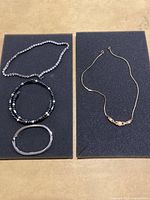 Overview of assorted bracelets and necklaces on dark foam background showing various styles and materials