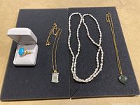 Full lot view showing the ring in a white box and three necklaces with different styles and pendants laid out on black padding.