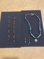 Turquoise bead necklace with silver-tone accents and a rectangular decorative pendant alongside matching earrings shown on dark foam board.