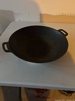 Heavy cast iron wok viewed from above on a white table.