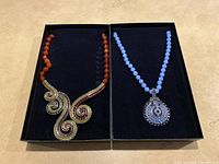 Two Heidi Daus necklaces side-by-side in black boxes, showing full necklaces and pendants.