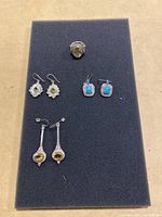Full set of four jewelry pieces arranged on a dark foam pad, including one ring and three pairs of earrings.