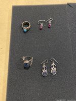 Overview of 2 rings and 2 pairs of earrings arranged on black foam.