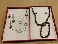 Full view showing two sets of costume jewelry in red boxes, one silver-tone geometric set with necklace and earrings and one brown faux pearl set with necklace, bracelet, and earrings