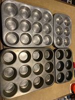 Set of four metal muffin tins arranged next to each other showing the different sizes and number of cup molds in each.