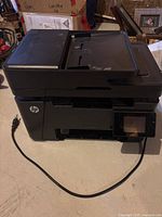 Front and top view of HP LaserJet Pro MFP M127fw printer showing scanner bed, paper trays, power cord, and control panel.