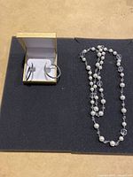 Long necklace with pearl and crystal beads laid out on black surface beside the earring box.