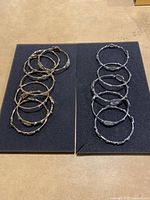 Two sets of metal bangles side by side on a black foam background, one gold-toned set and one silver-toned set, each with six bangles.