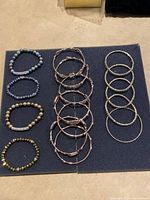 Overview photo showing all 15 bracelets arranged on a black display mat, including metal bangles and various beaded bracelets.