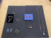 Full assortment of costume jewelry on black surface: multiple earrings, two rings, and two necklaces.