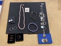 Full assortment of rings, earrings, and necklaces on black foam and beige surface showing the variety of jewelry included.