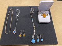 All jewelry pieces displayed on black foam, showing two necklaces, four pairs of earrings, and three pendants including one in jewelry box