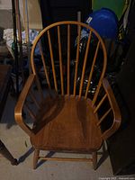 Wooden chair showing front view with rounded blade backrest with vertical spindles, cushioned seat, and armrests.