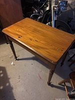 Angle view of wooden table showing the wood grain surface and one corner with one turned leg visible.