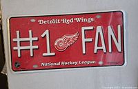 Front of license plate showing red background, white "#1 FAN" text, Detroit Red Wings logo, and NHL branding.