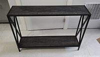 Full frontal view of wooden console table with black metal frame, two wooden shelves.