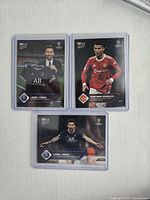 Front view of three football cards featuring Lionel Messi and Cristiano Ronaldo in protective sleeves.