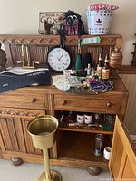 Full view of wooden cabinet with barware and collectibles displayed on and inside it, plus large brass-colored standing ashtray or umbrella stand.
