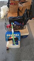 Image showing large white Igloo cooler with blue lid, small Styrofoam cooler, black wire basket with assorted items including hand bike pump on top of cooler.