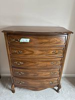 Front view of the wooden 5 drawer dresser showing curved drawers and metal handles, one handle missing.