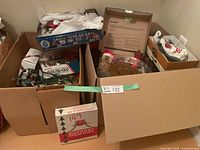 Two open boxes filled with various Christmas lights, tins, and decor pieces for sale.