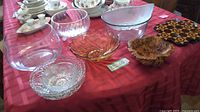 Display of seven glass bowls including clear glass, cut glass, flower-shaped orange bowl, and assorted sizes.