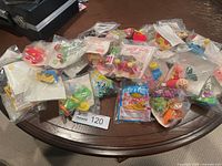 Overhead photo showing about twenty sealed McDonalds Happy Meal toys spread on a wooden table.