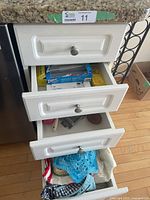 Three white drawers in kitchen setup containing various kitchen linens, food wraps, and utensils.