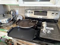 Kitchen appliances and cookware shown on stovetop and counter including electric fry pan, kettle, cookie sheet, and griddles