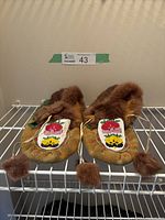 Top view of moccasins showing colorful floral beadwork and fur trim on tan leather base with fur pom pom laces.