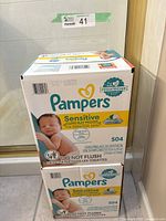Two unopened boxes of Pampers Sensitive baby wipes stacked one on top of the other in a tiled room.