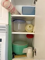Plastic kitchen containers including Tupperware of various colors stacked inside a kitchen cupboard.