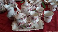 Overview of teapot, creamer, sugar bowl, tray, mugs and trinket box on red tablecloth
