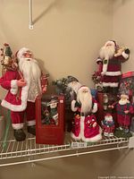 Wide view of all Santa figure decorations arranged on a shelf showing variety in size and style.