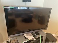 Sony Bravia 54 inch flat screen TV sitting on a stand, with two remotes and manuals on top.