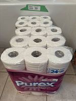 Multiple unopened packs of Purex toilet paper rolls stacked, showing packaging and label details.