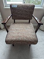 Front view of vintage rocking chair showing textured multi-tone upholstery and wooden arms.