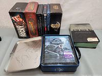 View showing all DVD and Blu-ray box sets in collection arranged upright and laid flat, including Rocky, Indiana Jones, Saturday Night Live, Star Wars Trilogy, Band of Brothers, and Jurassic World in a metal case.