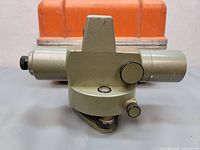 Geotec AL-23C auto level surveying transit shown from side, with visible adjustment knob and bubble level, placed in front of an orange carrying case.