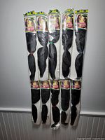 Ten packs of black Vega Braid hair extensions displayed hung in two rows against a white wall.