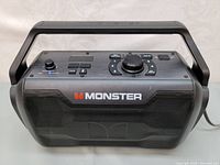 Front view of Monster Nomad speaker showing speaker grille with Monster logo and integrated carrying handle.