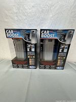 Two boxed Car Boost Portable Battery Jump Starters placed side by side showing front packaging with product information and images.