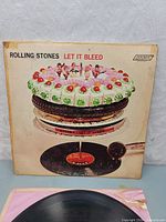 Album cover for Rolling Stones Let It Bleed showing front artwork with cake and record player imagery.
