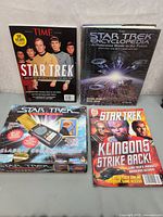 Four items including Star Trek Classic Communicator toy in original box, two Star Trek magazines, and hardcover Star Trek Encyclopedia book.