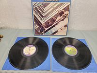 Photo of gatefold album cover with The Beatles looking down from a balcony, two vinyl records laid on blue paper beneath
