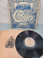 Vinyl LP record outside of cover with cover propped behind showing front artwork with ornate blue and sepia design and band member photos