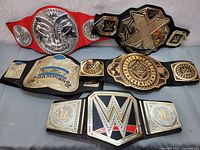 Full view of six WWE replica championship belts arranged on a surface showing details of designs and straps.