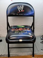 Front view of black folding chair showing WWE logo and SummerSlam 2000 promotional graphics on the backrest and seat.